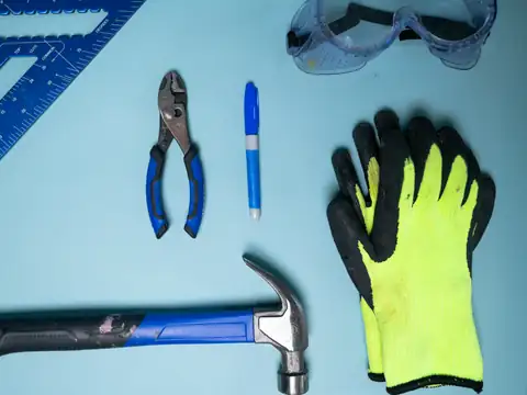 Hammer, pliers, marker and work gloves laid out on a bench